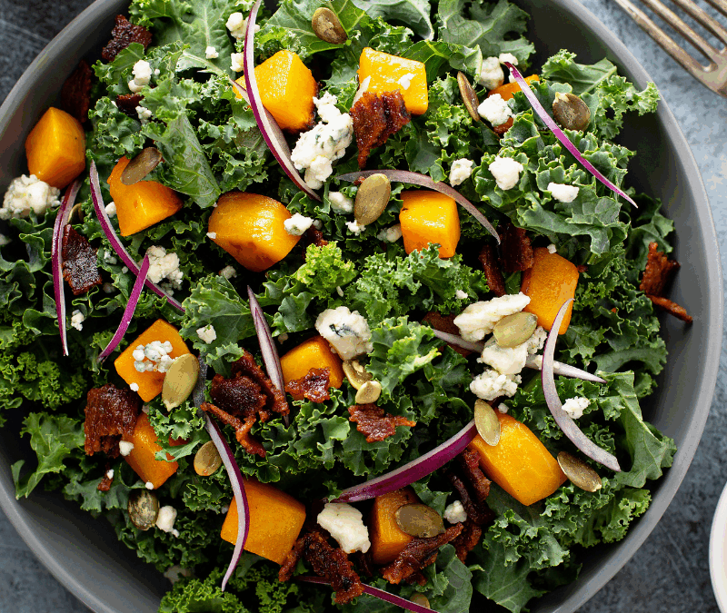 bowl filled with salad that includes kale, berries, squash, goat cheese, other fall foods.